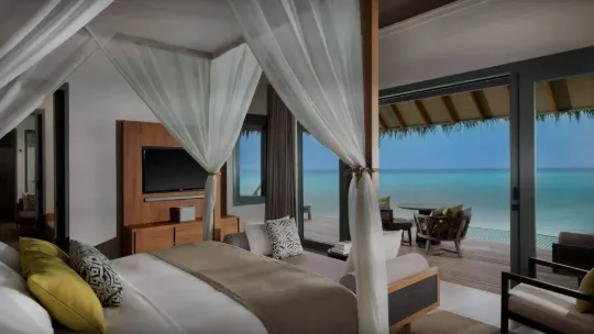 Overwater villa at Vakkaru Maldives resort featuring a four-poster canopy bed overlooking the ocean