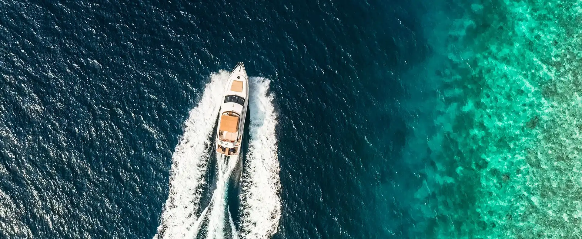 A yacht cruising through deep blue and turquoise tropical waters near a coral reef in the Maldives