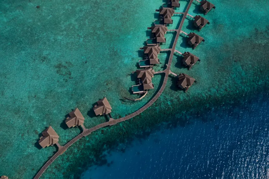 Overwater bungalows aligned along wooden jetties into turquoise ocean, Vakkaru Maldives Residence