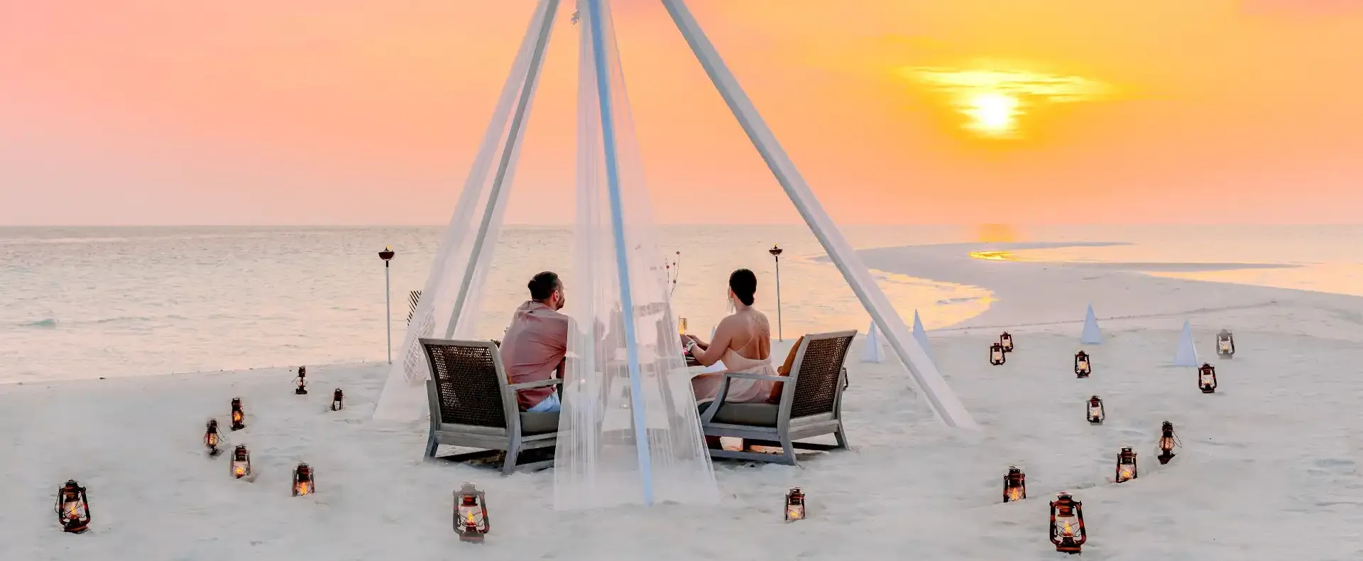 Romantic sunset beach dinner with lantern lighting.