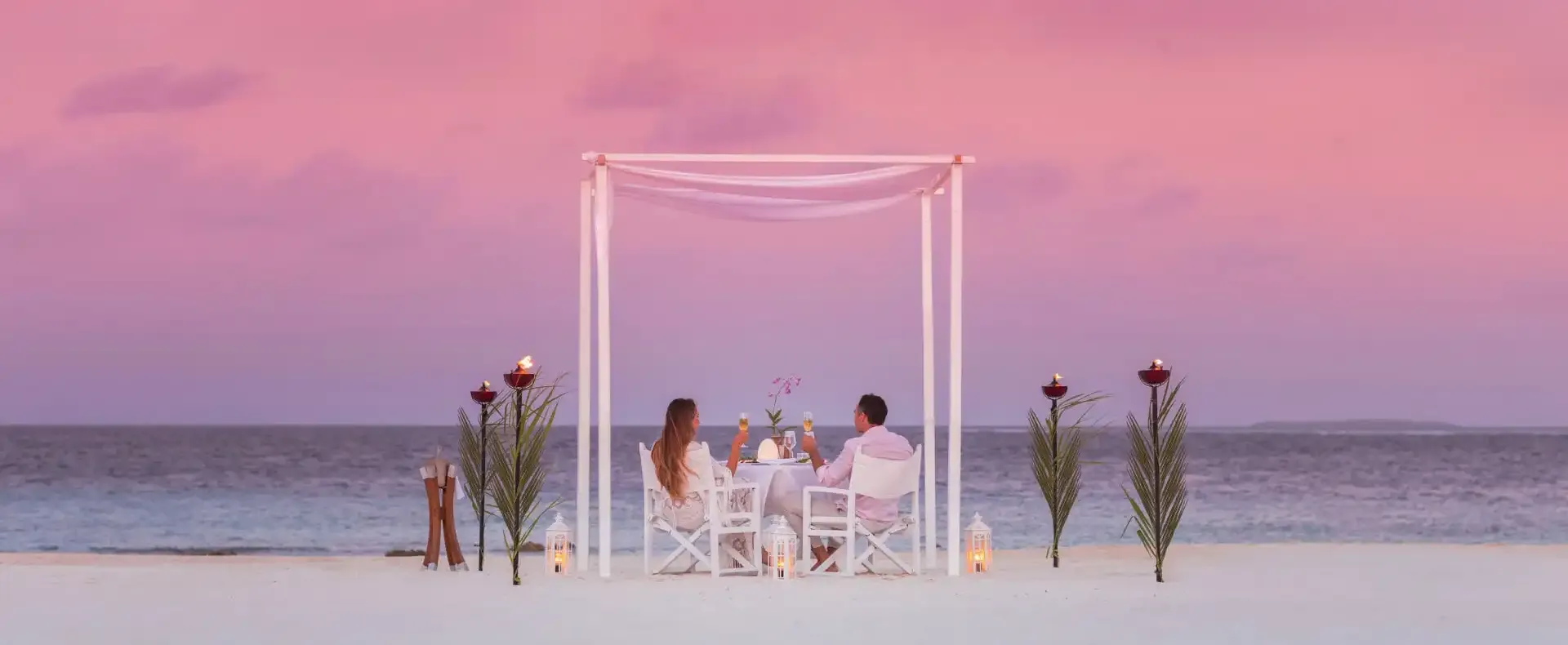 Couple enjoying romantic beach dinner with champagne at sunset.