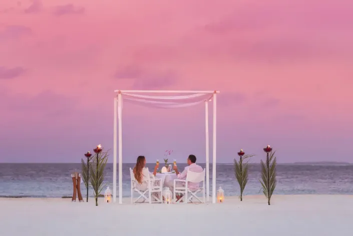 Candlelit beach dining at Vakkaru Maldives under a canopy at sunset.