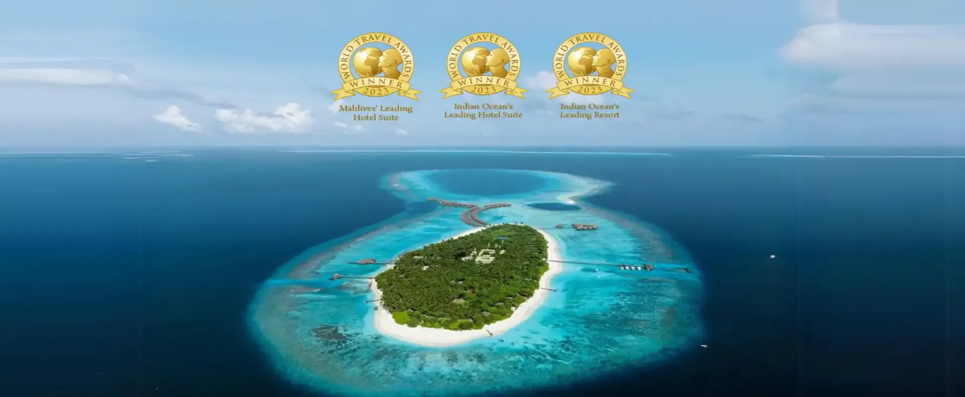 Aerial view of Maldives resort with overwater villas and reefs.