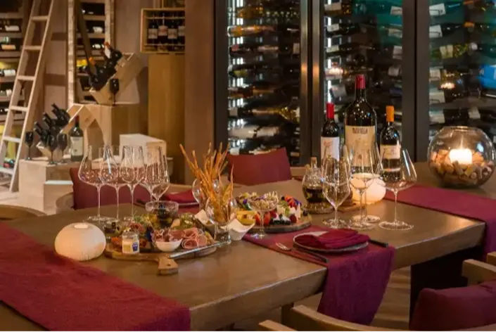 A long wooden dining table, lit by candles, stands amidst high-back chairs in an elegant wine cellar with walls full of bottles and glassware. Text: WINE, 2012, SOLAIA, TENUTA, CRUS.