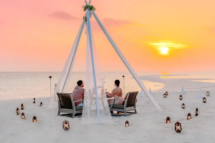 Romantic candlelit beach dining under canopy at sunset.