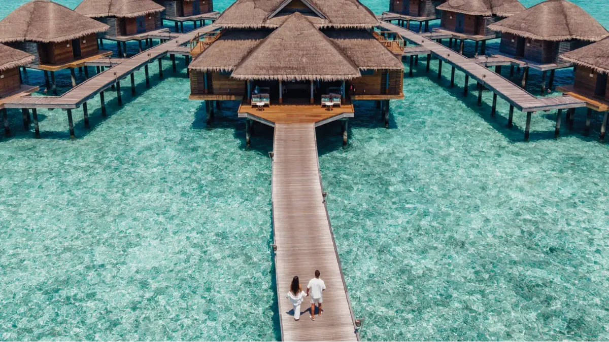 Couple strolling along an overwater jetty at Vakkaru Maldives towards luxurious overwater villas.