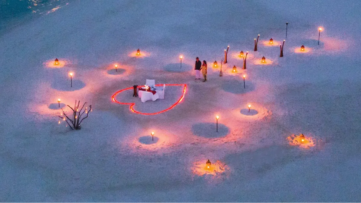 Romantic beach dinner at Vakkaru Maldives beneath illuminated heart-shaped lights beside the ocean.