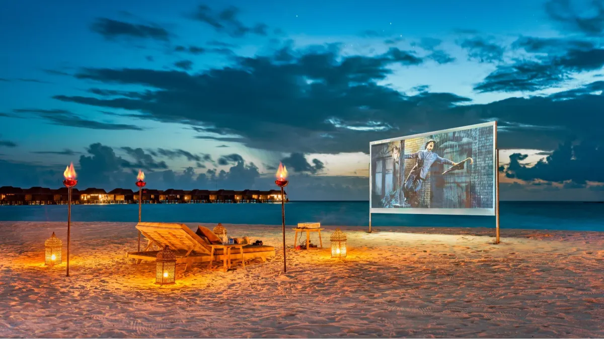 Beach cinema screen glowing at dusk over ocean, Vakkaru Maldives Residence