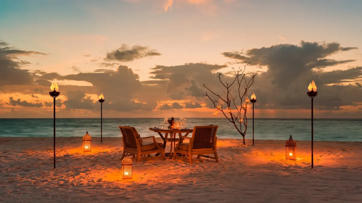 Beach dinner setup at sunset with lanterns and tiki torches, Vakkaru Maldives Residence