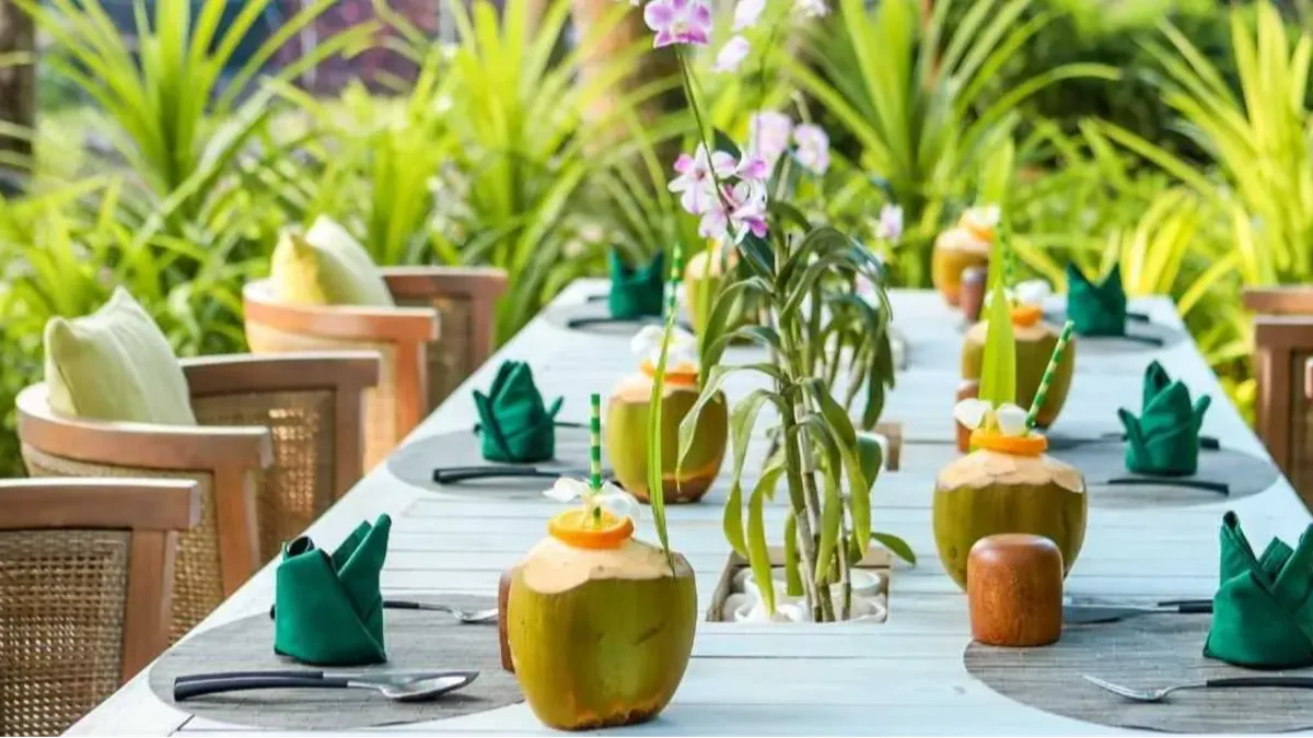 An outdoor dining table with coconuts and green napkins surrounded by lush tropical plants, Vakkaru Maldives Residence