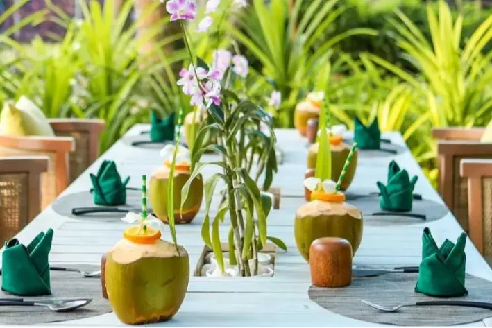 Garden dining setup at Vakkaru Maldives decorated with coconuts and orchids.