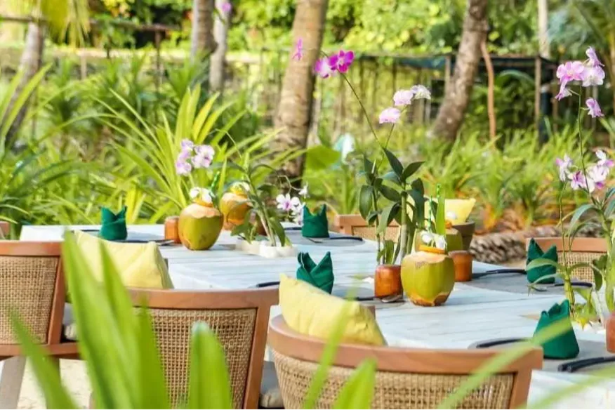 Garden dining setup at Vakkaru Maldives decorated with coconuts and orchids.