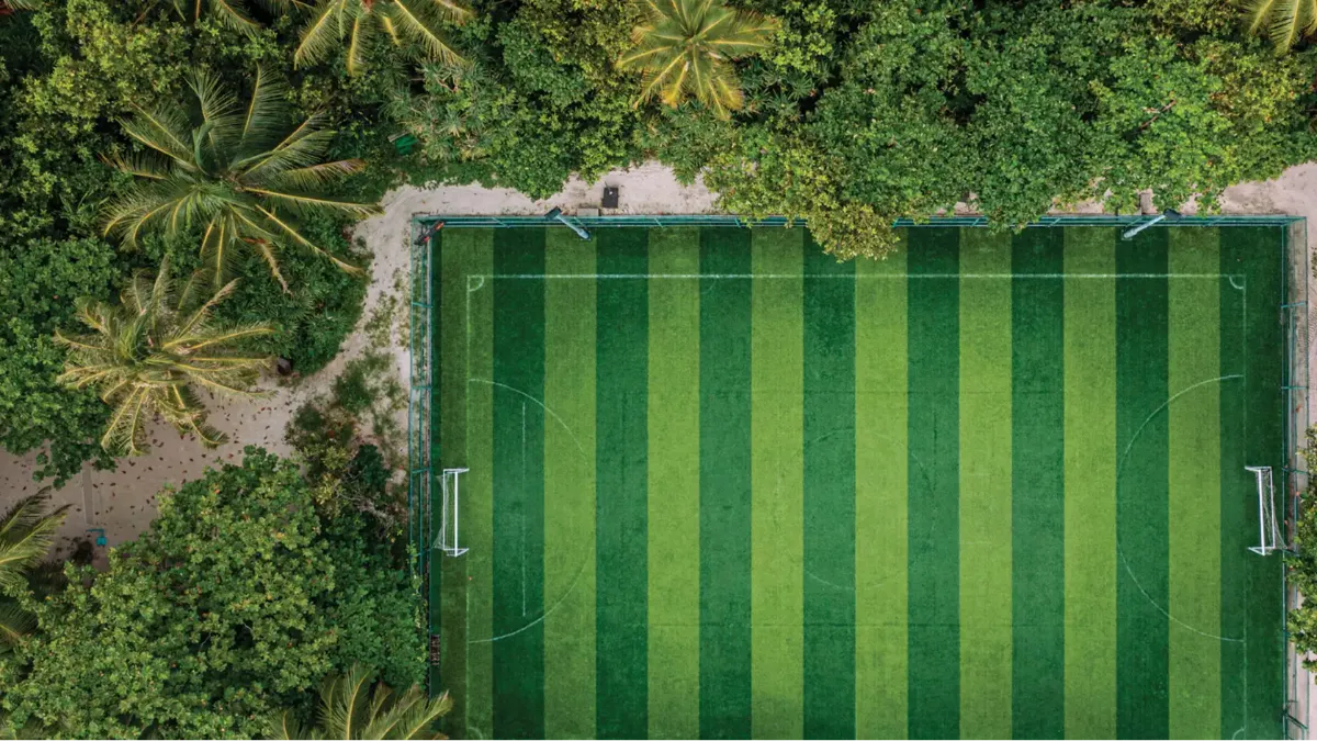 Aerial view of a striped green soccer field bordered by forest and sand paths, Vakkaru Maldives Residence resort